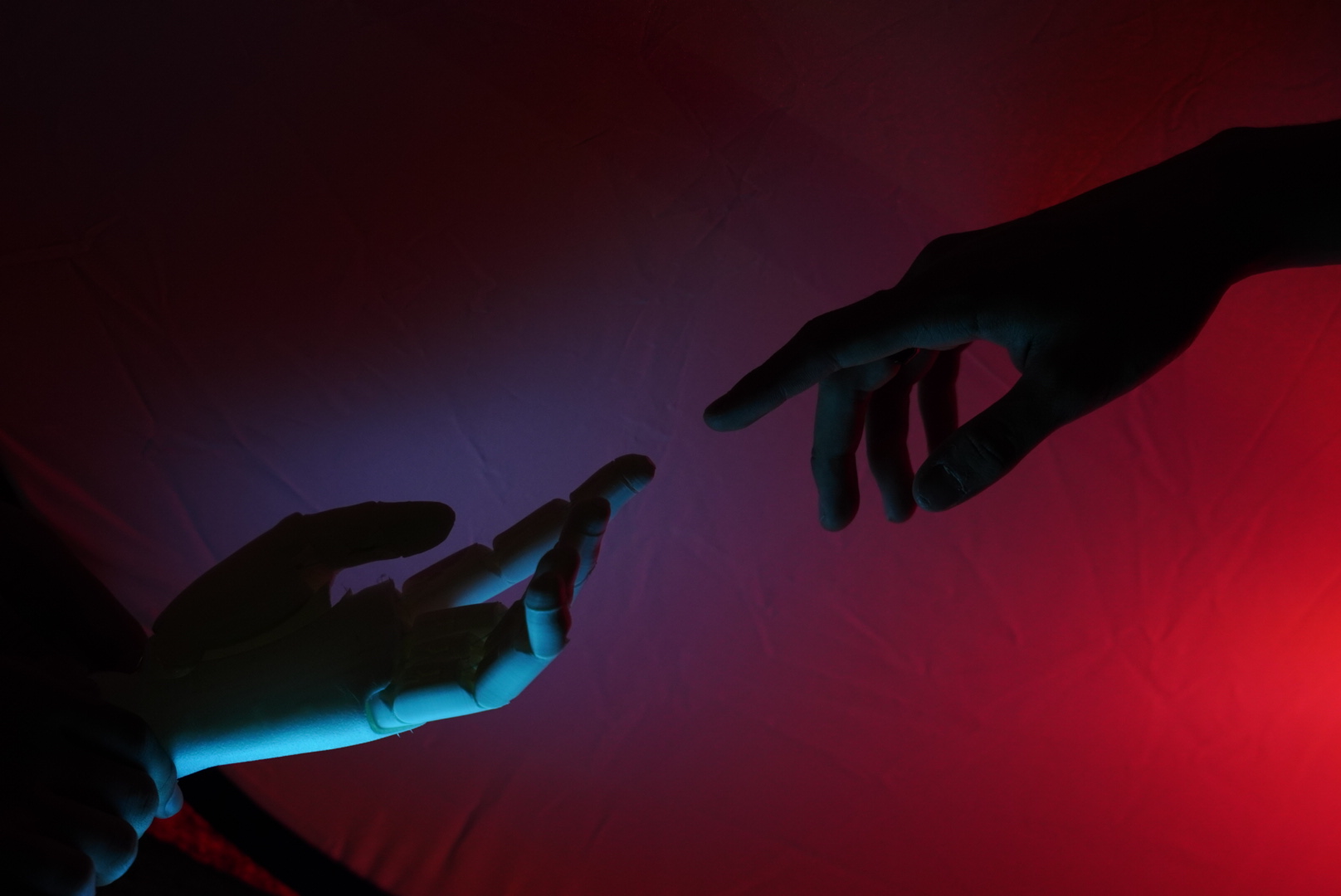 A human hand reaching towards a prosthetic hand under red and blue lighting